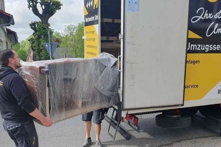 zwei umzugshelfer laden verpacktes moebel in umzugswagen